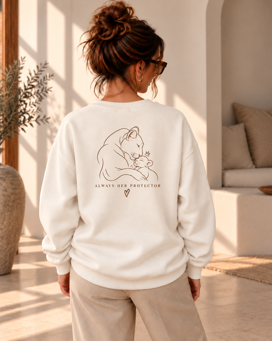 Achteraanzicht van een vrouw in een ivoorkleurige oversized trui met rugprint van een leeuwin met welpje en “ALWAYS HER PROTECTOR”
