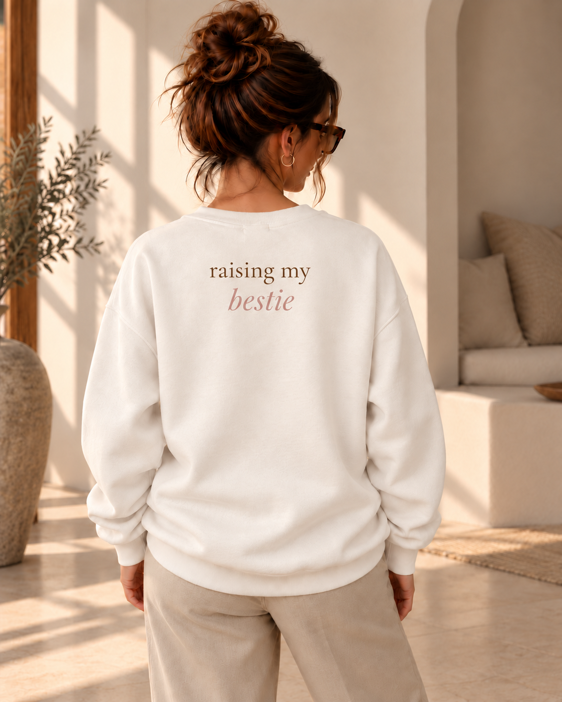 Achteraanzicht van een vrouw in een ivoorkleurige oversized trui met rugprint “raising my bestie”